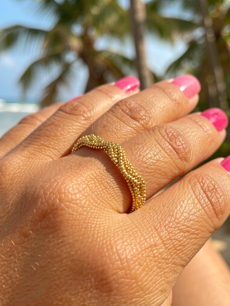 Anel de ouro com miçangas em mão feminina com esmalte rosa vibrante, luz natural e fundo desfocado.