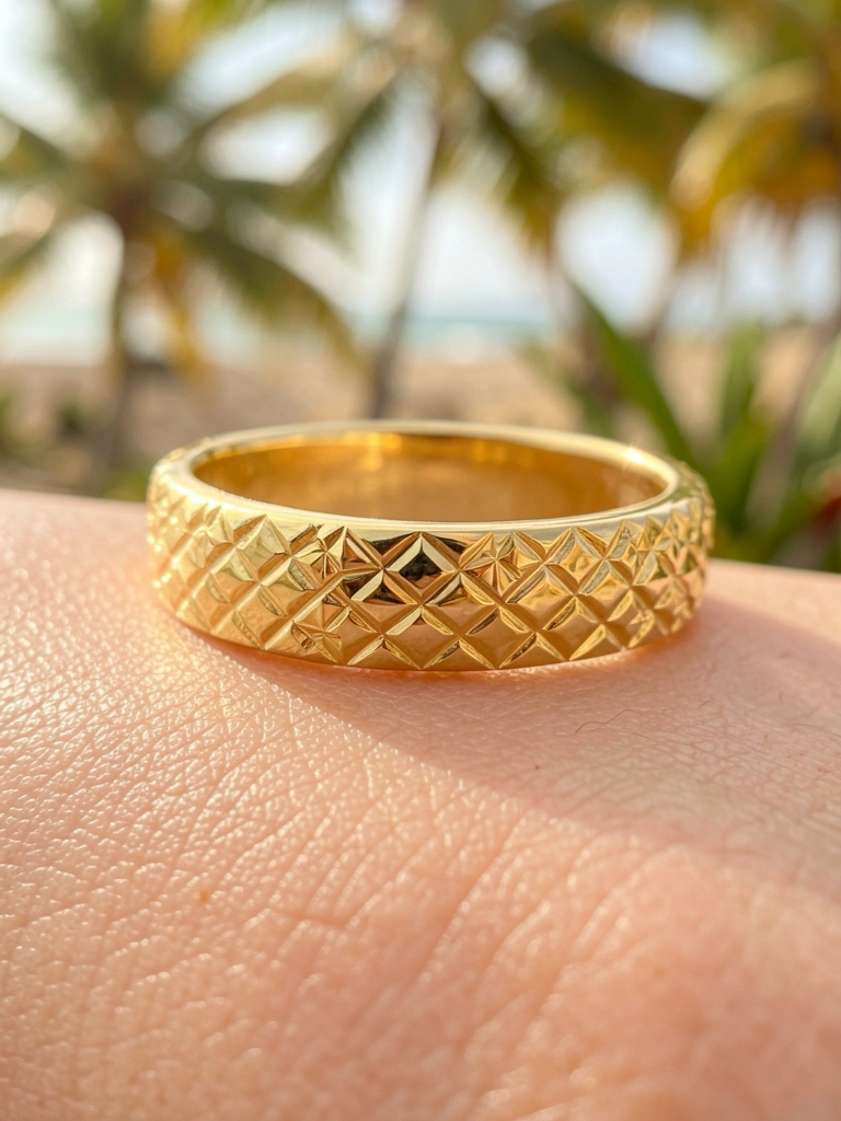 Anel de ouro amarelo brilhante com padrão de losangos gravados, luz natural difusa e folhagem tropical desfocada ao fundo.