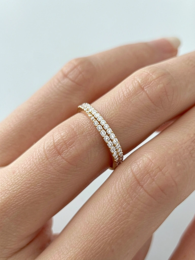 Anel de ouro com diamantes brilhantes segurado por mão com esmalte claro, fundo cinza desfocado e luz difusa.
