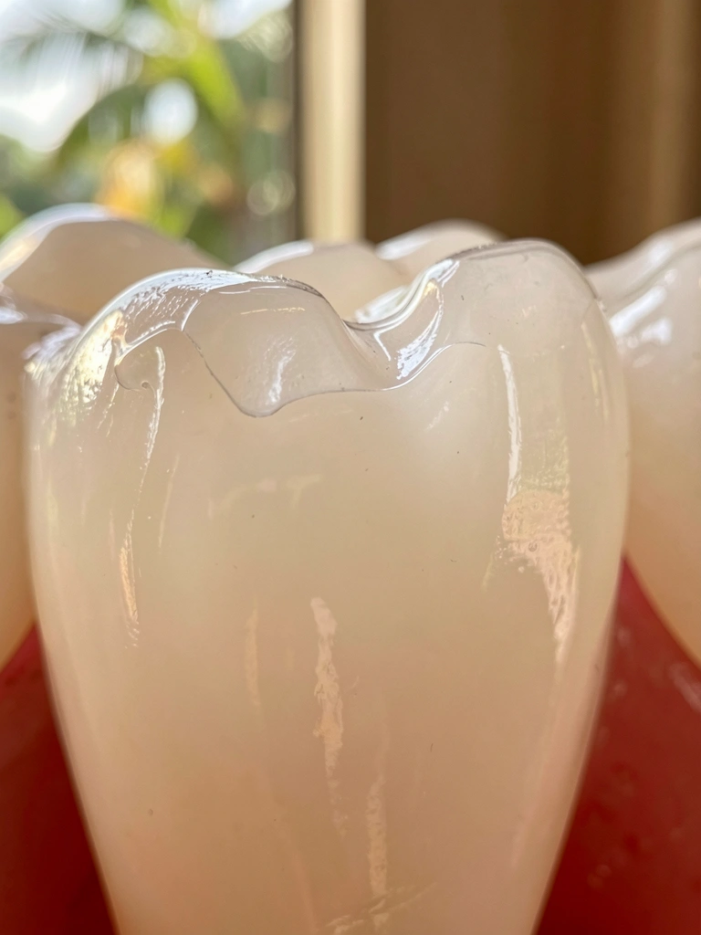 Close extremo de dente branco perolado com selante dental transparente na superfície de mordida, luz natural difusa e fundo desfocado.