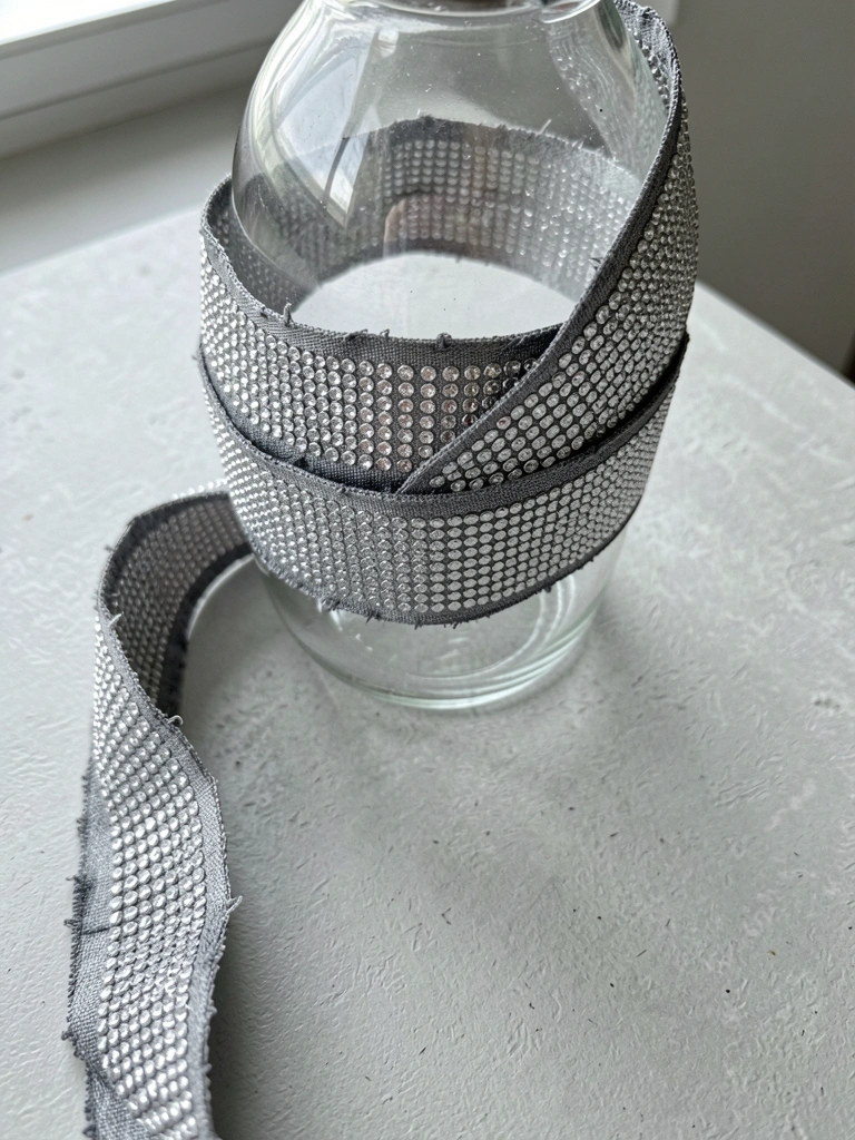 Vaso de vidro transparente com fita de strass prateada sobre mesa de madeira clara
