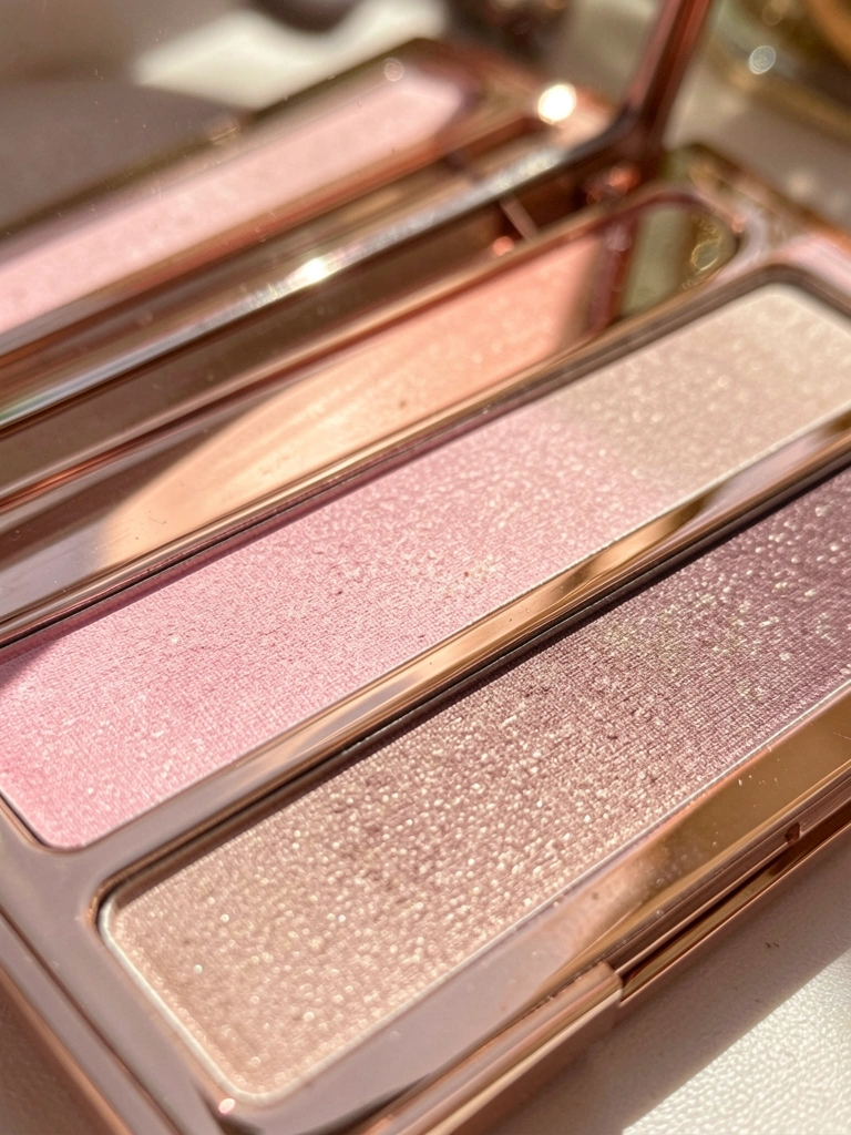 Paleta de sombras em estojo espelhado com tons de rosa, nude e bege, luz natural suave e fundo desfocado.