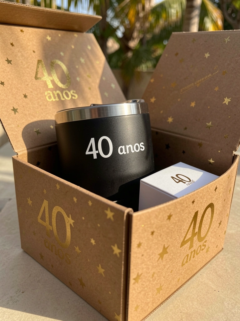 Caixa de papelão marrom com estampa dourada de estrelas, abrigando um copo térmico preto e uma caixa branca menor, sob luz natural.